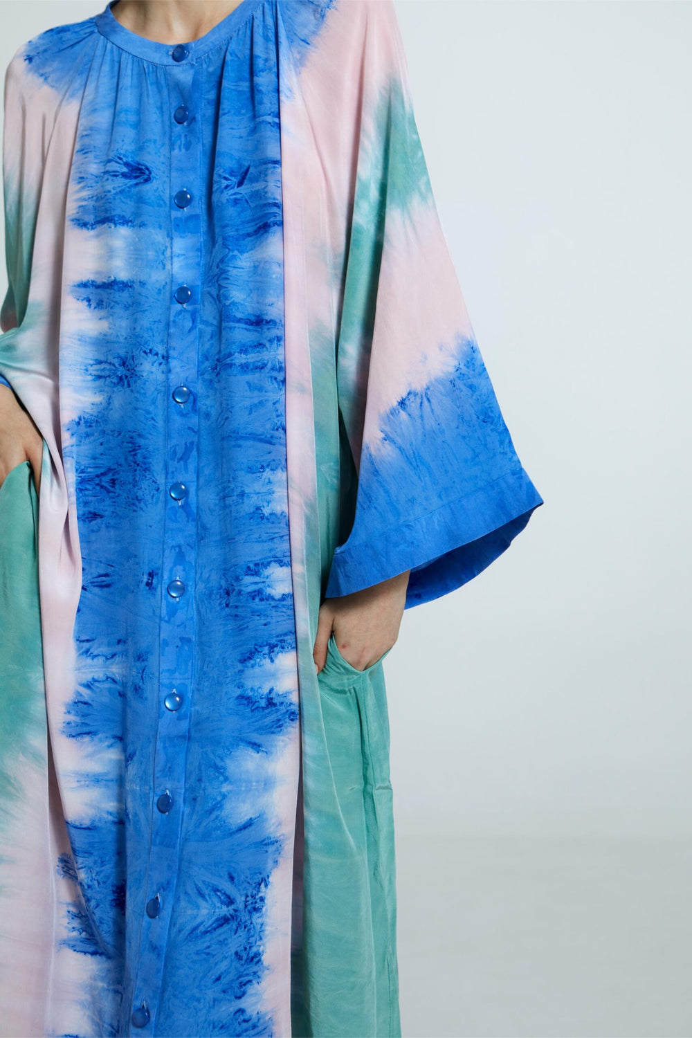 Vestido amplo de seda com padronagem tie-dye artesanal em tons vibrantes de azul, verde e rosa. Manga ampla e caimento solto.